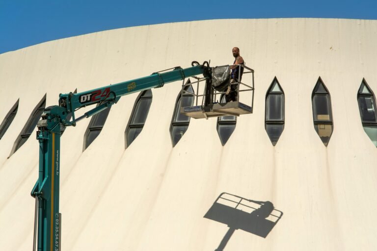 A worker on an aerial lift operates near a modern building facade with unique windows.